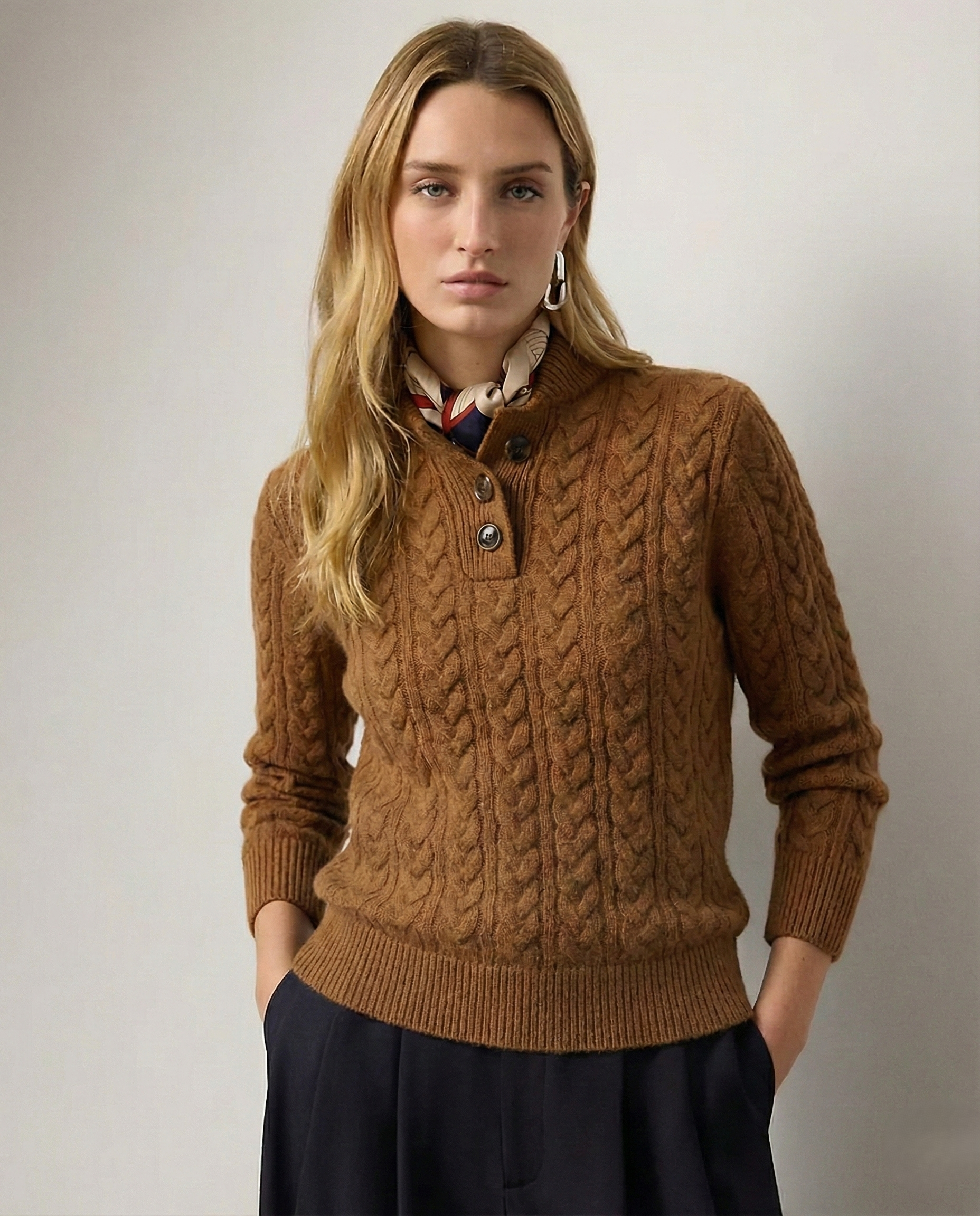 Woman wearing a brown cable knit sweater against a plain background