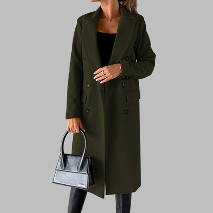 Vrouw in olijfgroene winterjas met dubbele knopen, zwarte handtas en zwarte laarzen tegen een grijze achtergrond. Stijlvolle damesmode.