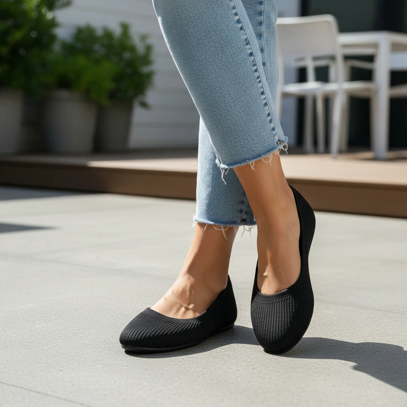 Person wearing black flats and light blue jeans on a concrete surface with blurred outdoor background