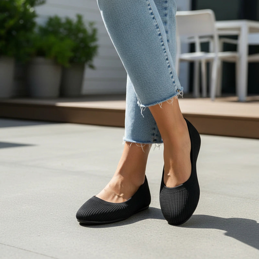 Person wearing black flats and light blue jeans on a concrete surface with blurred outdoor background