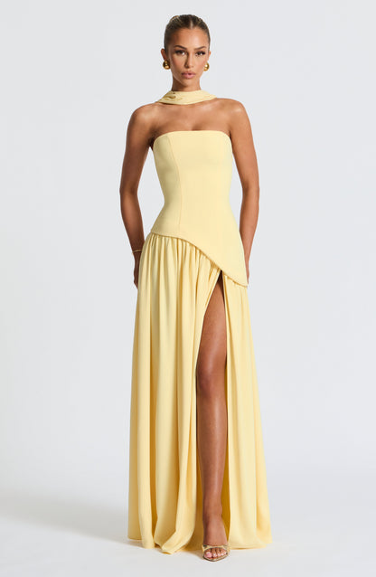Woman wearing a yellow strapless gown with a slit on a white background